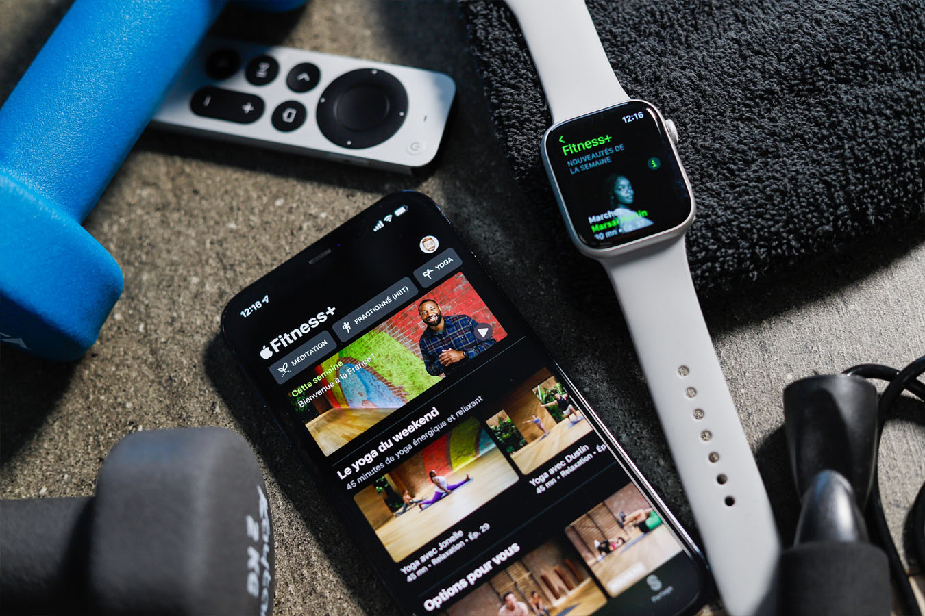 iPhone with the Apple Fitness+ app open, accompanied by sports accessories, an Apple Watch, and an Apple TV remote placed nearby. ©2021 Mathieu Improvisato